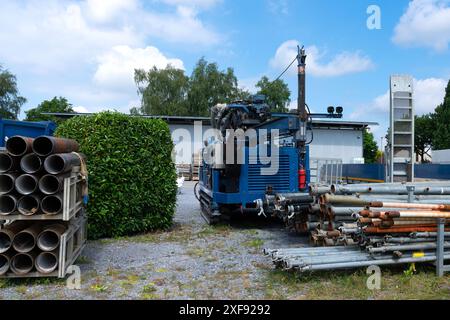 Eine blaue Bohrmaschine steht im Leerlauf auf einem Bauhof. In der Nähe befinden sich gestapelte Rohre, Metallstangen. Stockfoto