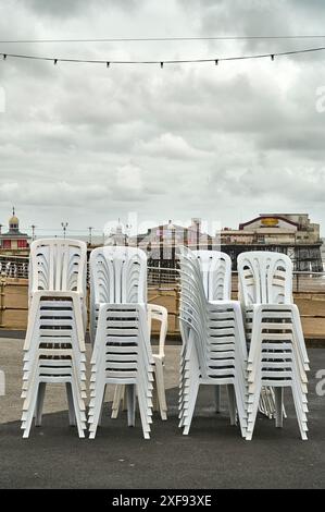 Weiße Plastikstühle stapelten sich an einem kalten grauen Tag im Sommer an der Küste von Blackpool Stockfoto