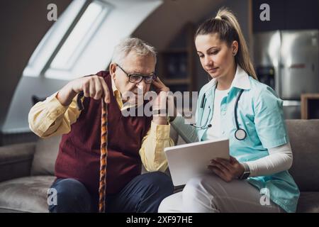 Hausarzt besucht Senioren, um seine Gesundheit zu überprüfen. Professionelle Pflegekraft hilft dem alten Mann zu Hause. Stockfoto