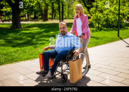 Ein Mann im Rollstuhl geht vom Einkaufen. Sein Freund hilft ihm beim Rollstuhl. Stockfoto