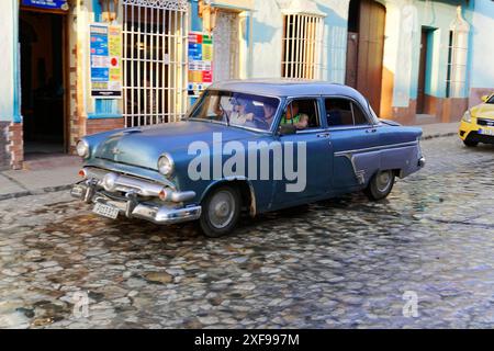 Trinidad, Kuba, Grosse Antillen, Karibik, Mittelamerika, Amerika, blauer Oldtimer, der auf einer Kopfsteinpflasterstraße vor historischen Gebäuden fährt Stockfoto