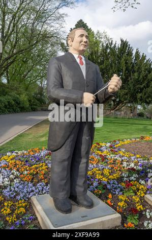 Die Statue eines Mannes im dunklen Anzug mit einem Dirigenten steht vor einem bunten Blumenbeet in einem Park, Skulpturen in Siegen Stockfoto