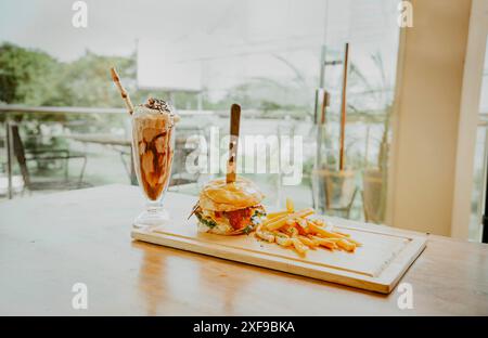 Nahaufnahme eines Burgers mit Pommes und Milchshake auf Holzbrett mit Platz für Text. Leckerer großer Burger mit Pommes frites und Milchshake im Restaurant Stockfoto