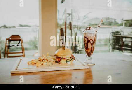 Leckerer großer Burger mit Pommes frites und Milchshake auf dem Restauranttisch. Nahaufnahme eines Burgers mit Pommes und Milchshake auf Holzbrett mit Platz für Stockfoto