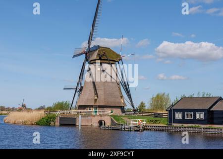 Windmühle an einem ruhigen Fluss, neben einem kleinen Haus, unter einem klaren blauen Himmel, kinderdijk, niederlande Stockfoto
