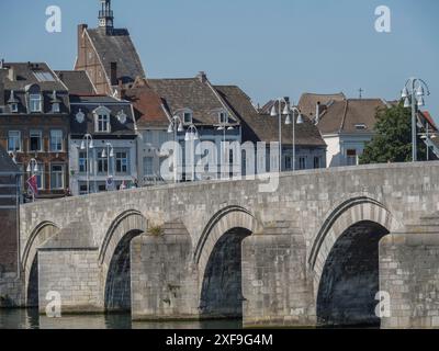 Steinbrücke über einen Fluss, umgeben von alten Stadthäusern und Lampen bei Tageslicht, maastricht, niederlande Stockfoto