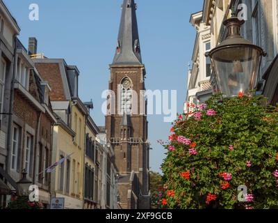 Ein malerisches historisches Zentrum mit einem großen Kirchturm, umgeben von alten Häusern und blühenden Blumen, maastricht, niederlande Stockfoto