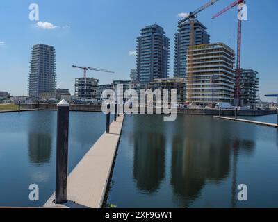 Moderne Wolkenkratzer und Baukräne spiegeln sich in einem ruhigen Hafen unter klarem Himmel in oostende, belgien, wider Stockfoto