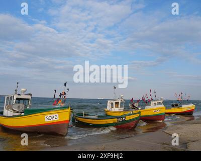 Mehrere bunte Fischerboote in einer Reihe am Strand, ruhiges Meer und bewölkter Himmel, sopot, ostsee, polen Stockfoto
