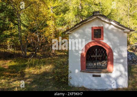 Eine kleine weiße Kapelle mit rotem Fensterrahmen am Waldrand im Herbstlicht, saas Fee, schweiz Stockfoto