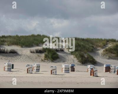 Liegestühle verstreut an einem Sandstrand vor grasbewachsenen Dünen unter bewölktem Himmel, Spiekeroog, Nordsee, deutschland Stockfoto