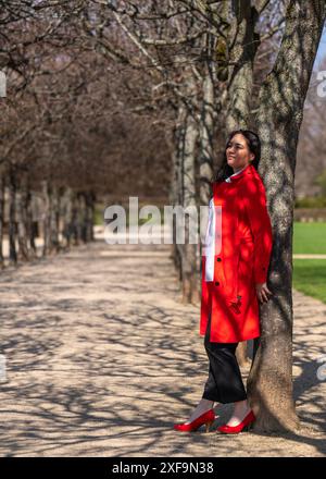 Porträt einer Frau mit dunklem Haar in rotem Regenmantel und Geschäftsbluse. Er steht unter freiem Himmel und blickt nachdenklich in die Ferne Stockfoto