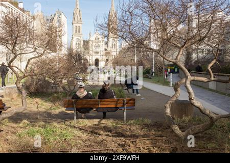 Die Menschen entspannen sich zwischen den Bäumen im Jardin Truillot an einem schönen sonnigen Tag in Paris, Frankreich. Im Hintergrund befindet sich die Kirche Saint-Ambroise. Stockfoto