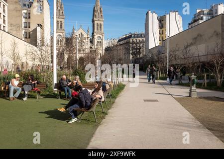 Pariser entspannen in der Sonne im Jardin Truillot an einem schönen sonnigen Tag in Paris, Frankreich. Im Hintergrund befindet sich die Kirche Saint-Ambroise. Stockfoto