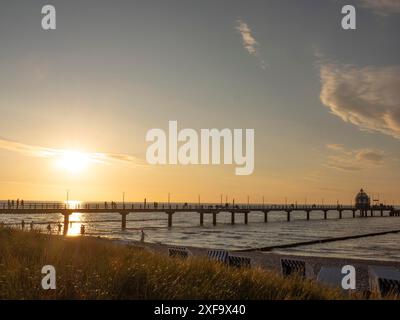 Ein Steg im Meer bei Sonnenuntergang, die Sonne färbt Himmel und Wasser in warmen Tönen, Zingst, ostsee, deutschland Stockfoto