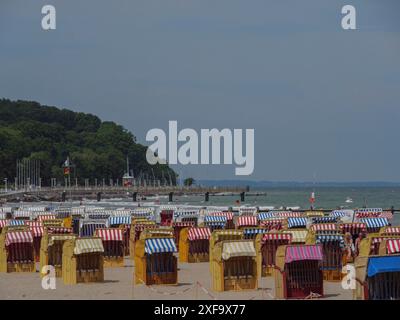 Strand voller farbenfroher Liegen mit Blick auf das Meer und die bewaldete Küste unter klarem Himmel, lübeck, Ostsee, Deutschland Stockfoto