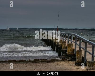 Holzsteg führt ins Meer, ruhige Wellen krachen gegen das Ufer, Boote im Hintergrund, lübeck, Ostsee, Deutschland Stockfoto