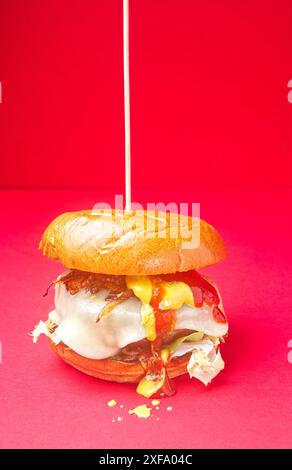 Asturischer Beef Burger. Burger Brioche Brot, Zwiebeln, Becom Käse, Senf, Ketchup, auf rotem Hintergrund. Spanien Stockfoto