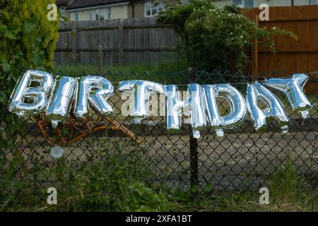 Silberne Happy Birthday-Worte aus aufblasbaren Ballons am Gartenzaun in england großbritannien. Stockfoto