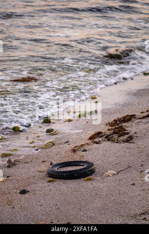 Alte Autoreifen am Strand, Wasser und Meeresküste Verschmutzung Autoreifen am Sandstrand, ein Bild von einem alten Autoreifen, der in den Sand eingewachsen ist. Alte Autoreifen mit Stockfoto