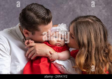 Der junge Vater und die Mutter küssen ihr kleines Mädchen zärtlich. Liebe und Zärtlichkeit der Eltern. Hochformat. Nahaufnahme Stockfoto