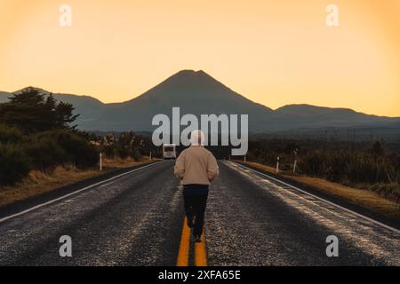 Rückansicht der weiblichen Touristen, die auf der Straße mit dem vulkanischen Mount Ngauruhoe am Morgen im Tongariro-Nationalpark, Neuseeland, laufen Stockfoto