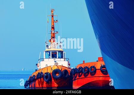 Orangene Boote legen nebeneinander im Wasser an. Die Boote sind groß und haben einen weißen Streifen. Das Wasser ist ruhig und der Himmel ist klar Stockfoto