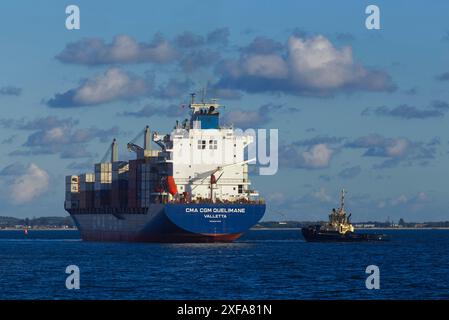 Ein großes Containerschiff wird von einem Schlepper im Hafen von Sydney, New South Wales, Australien, unterstützt. Stockfoto
