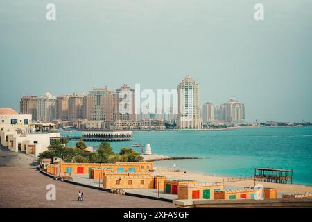 Panoramablick auf moderne Hochhäuser entlang der Uferpromenade in Doha, Katar, mit klarem Himmel und türkisfarbenem Wasser Stockfoto