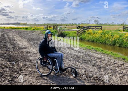 Eine junge Frau im Rollstuhl läuft auf einer schwierigen Straße auf dem Land Stockfoto