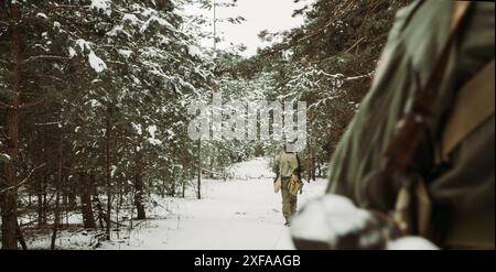 Amerikanischer Infanterie-Soldat, Der Am Kalten Wintertag Durch Die Forest Road Fährt. Gruppe von US-Soldaten marschiert auf der Landstraße. Soldaten Der Us-Armee Des Weltkriegs Stockfoto