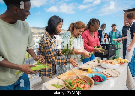 Generationenübergreifende Menschen, die auf dem Dach des Hauses grillen - multirassische Freunde, die am Wochenende Spaß beim Essen und Kochen haben - Sommer und Stockfoto