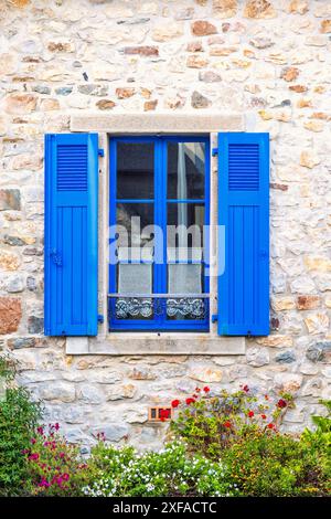 Idyllisches Ferienhaus mit einem Fenster und blauen Fensterläden in einem Garten mit Blumen Stockfoto