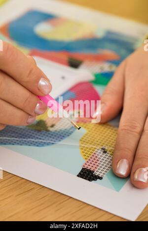 Eine Nahaufnahme einer Hand, die Kristalle auf einer Leinwand für ein Diamantmalprojekt platziert. Diamantmosaik Stockfoto