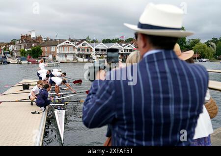 Die Menschen blicken von der Seite des Flusses aus, während sich eine Rudermannschaft von einem Ponton aus auf den Weg zur Startlinie macht, am Eröffnungstag der Henley Royal Regatta 2024 entlang der Themse in Henley-on-Thames, Oxfordshire. Bilddatum: Dienstag, 2. Juli 2024. Stockfoto