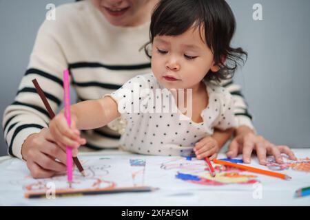 Kleinkind-Baby-Training zum Zeichnen mit Buntstift mit Mutter, die auf dem Tisch hilft Stockfoto