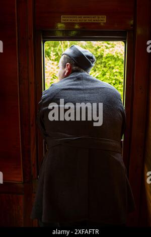 Rückansicht des abgelegenen männlichen Re-Enacto aus den 1940er Jahren in RAF-Kostüm, das in einem alten Eisenbahnwaggon an Bord der Severn Valley Heritage Railway, Großbritannien, aus dem Fenster gebeugt ist. Stockfoto