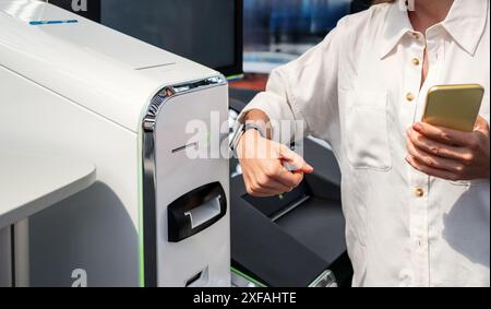 Konzept der Nahfeldkommunikationstechnik. Eine Geschäftsfrau verwendet ihre Smart Watch und ihr Smartphone, um am Flughafen oder Bahnhof für ein Ticket zu bezahlen. Stockfoto