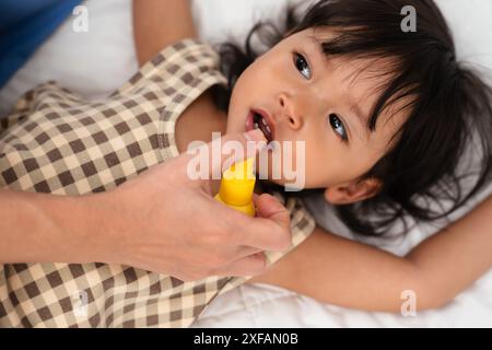 Mutter oder Arzt sprüht Medikamente im Mund eines Kleinkindes. Behandlungskonzept für Baby-Halsschmerzen Stockfoto