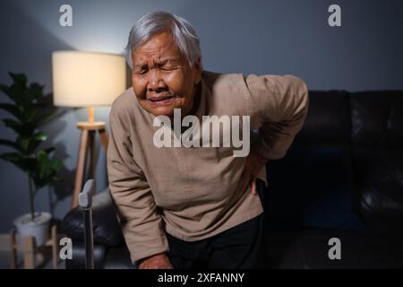 Ältere Frau, die nachts im Wohnzimmer unter Schmerzen im unteren Rücken leidet Stockfoto