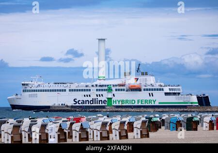 Rostock, Deutschland. Juli 2024. Hinter leeren Liegestühlen am Warnemünde-Strand fährt die Fähre 'Kopenhagen' auf der Ostsee in Richtung Dänemark. Kalt, windig und mit starken Regenschauern zeigt das Sommerwetter in Norddeutschland derzeit seine unfreundliche Seite. Quelle: Jens Büttner/dpa/Alamy Live News Stockfoto