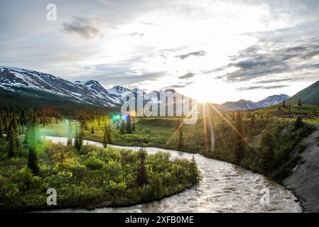 Atemberaubender kanadischer Sonnenuntergang mit schneebedeckten Bergen und Fluss in Schuss. Im Sommer auf der North Canol Road im Yukon-Territorium im Norden Kanadas. Stockfoto