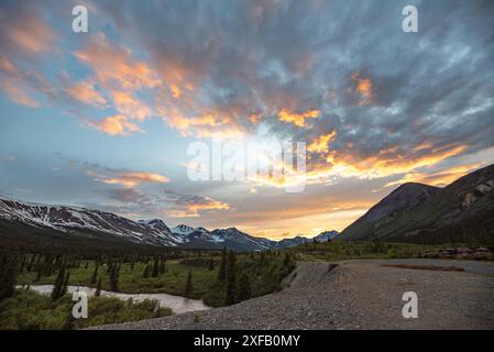 Atemberaubender kanadischer Sonnenuntergang mit schneebedeckten Bergen und Fluss in Schuss. Im Sommer auf der North Canol Road im Yukon-Territorium im Norden Kanadas. Stockfoto