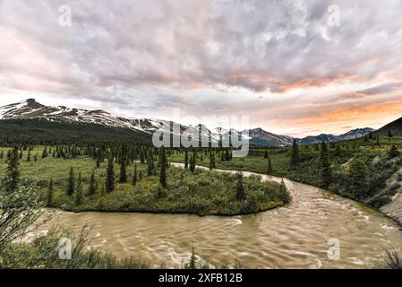 Atemberaubender kanadischer Sonnenuntergang mit schneebedeckten Bergen und Fluss in Schuss. Im Sommer auf der North Canol Road im Yukon-Territorium im Norden Kanadas. Stockfoto