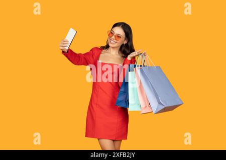 Junge Frau im roten Kleid, die Selfie mit Einkaufstaschen nimmt Stockfoto