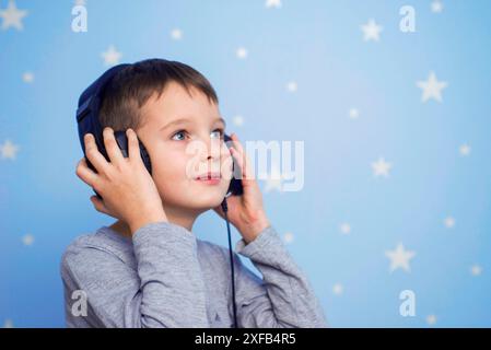 Ihr Kind hört gern Musik über Kopfhörer auf blauem Hintergrund mit Sternen Stockfoto