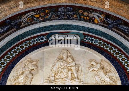 Madonna und Kind flankiert von Engeln mit gefalteten Armen, Duomo di Santa Maria Assunta auf dem Campo dei Miracoli in Pisa, Toskana, Italien. Marmor-Lünette der Portale di San Ranieri oder Tor von San Rieri, einst an der Westfassade, aber nach einem Brand im Jahr 1595 auf die Ostseite des Südquerschiffs verschoben. Stockfoto