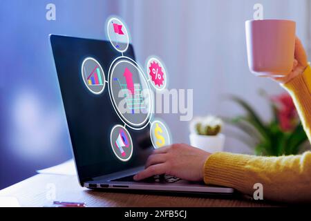 Nahaufnahme einer Person, die Online-Shopping-Daten auf einem Laptop analysiert, während sie eine Kaffeetasse hält. Auf dem Bildschirm werden verschiedene E-Commerce-Symbole angezeigt, die darstellen Stockfoto