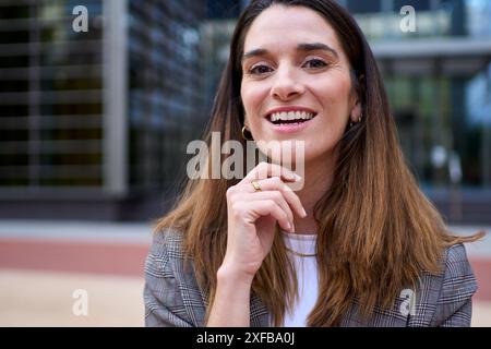 Lächelnde weiße Geschäftsfrau mittleren Alters posiert mit Hand am Kinn Stockfoto