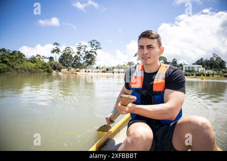 Lächelnder Mann in Schwimmweste, der auf einem kleinen See paddelt Stockfoto